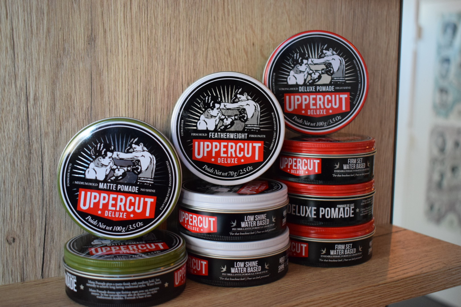 Een stapel blikjes Uppercut Deluxe pomade op een houten plank