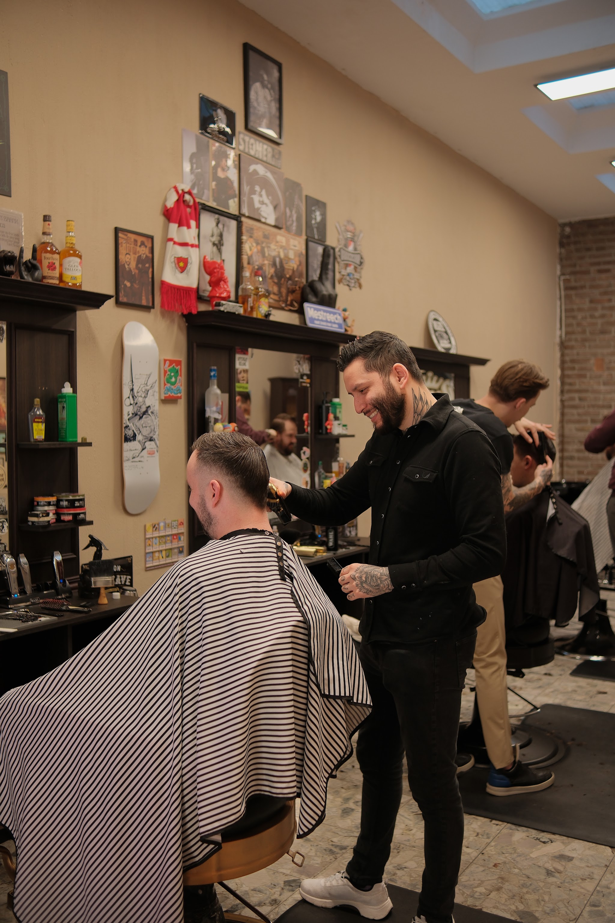 Een barber aan het werk bij een klant onder een gestreepte kapmantel, met de shop op de achtergrond