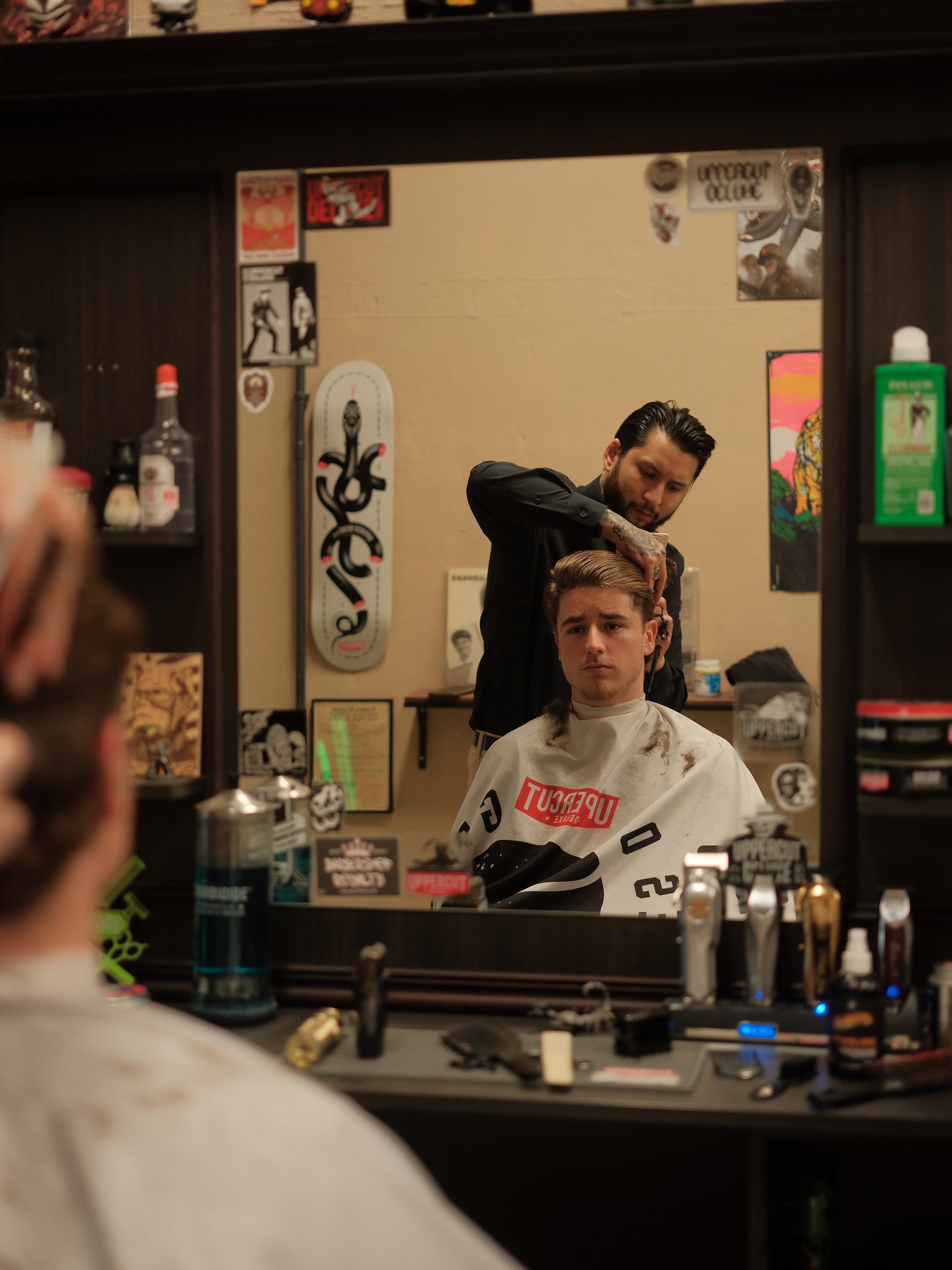 Een barber knipt een jonge klant, gezien in de spiegel met een skateboard aan de muur