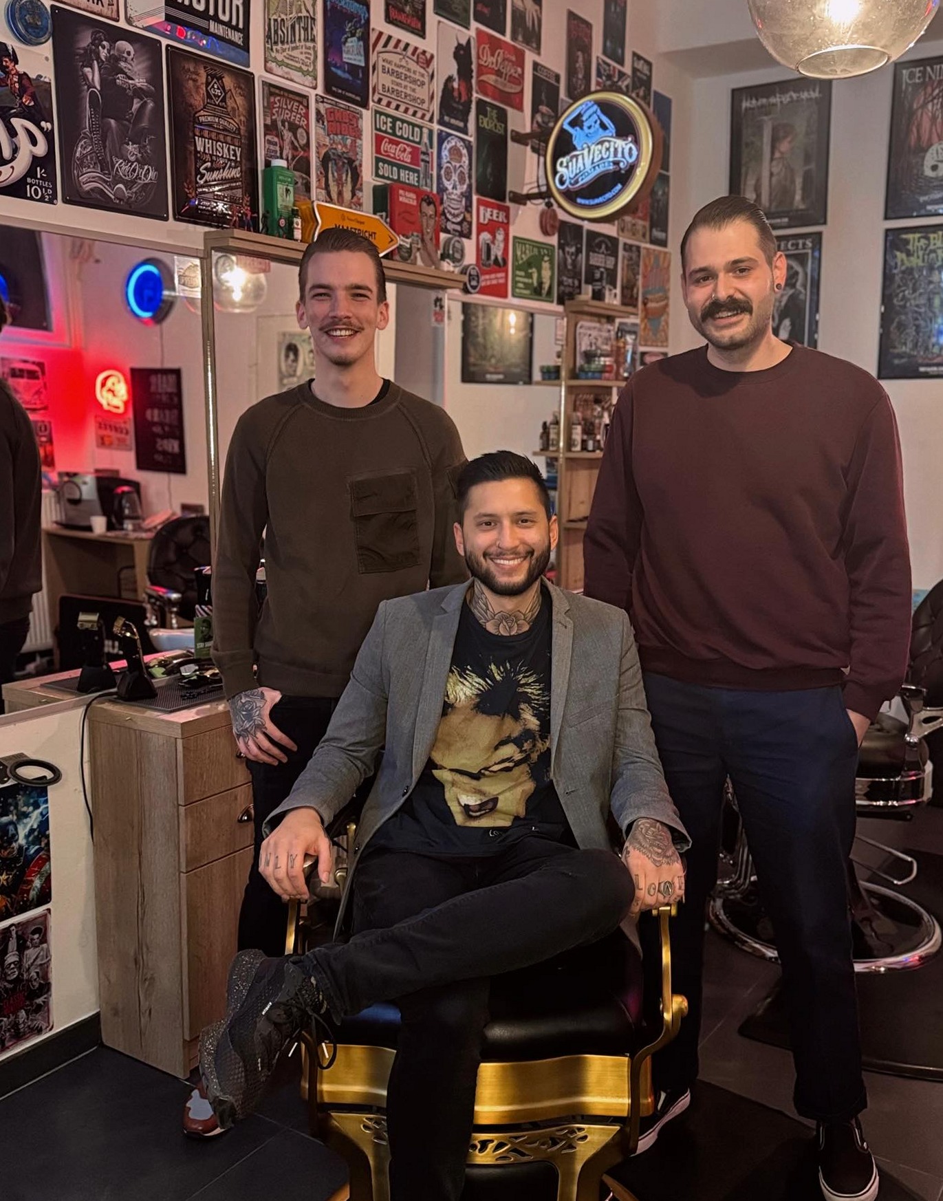 Drie mannen van het team in de shop, een van hen in de gouden barberstoel
